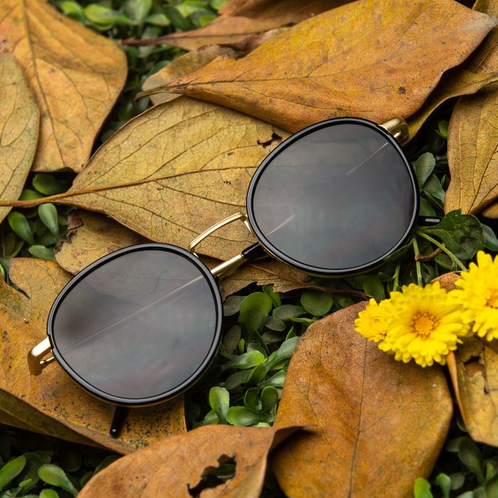 Elegant sunglasses resting on dry autumn leaves with bright yellow flowers for a chic fall vibe.