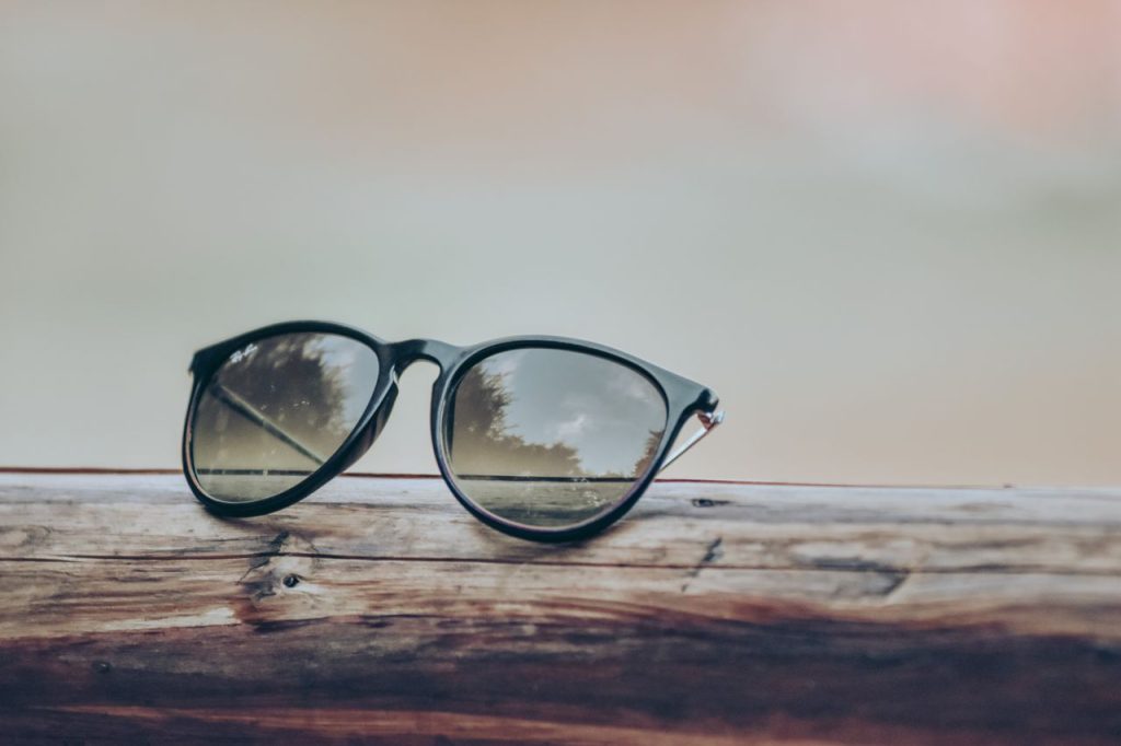 Stylish sunglasses resting on a wooden surface, reflecting nature.