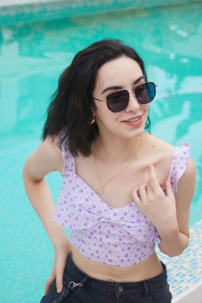 Elegant woman in sunglasses poses by a pool, showcasing summer fashion.