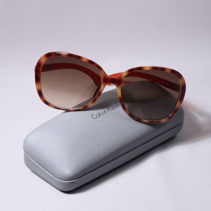 Elegant tortoiseshell sunglasses with brown lenses on a branded gray case.