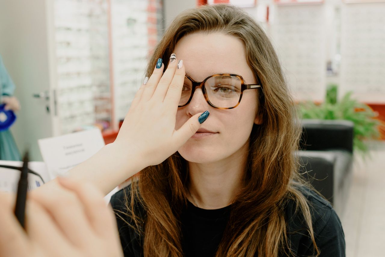 services-01 Focused female patient looking at hand of unrecognizable ophthalmologist while checking eyesight in new eyeglasses during appointment in clinic on blurred background